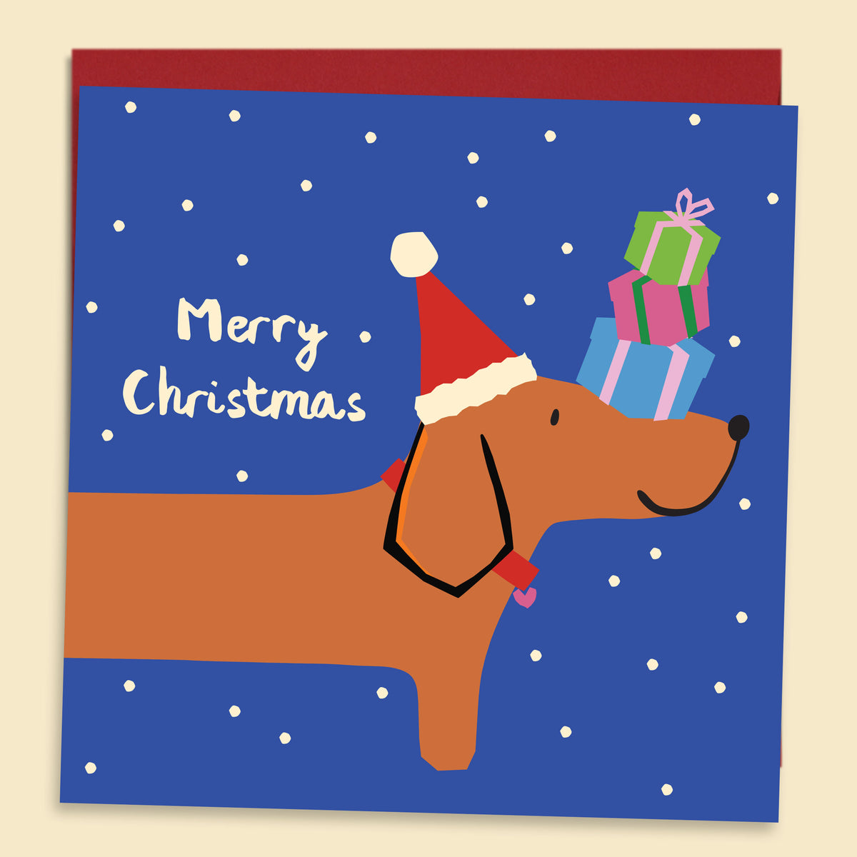 A Christmas greeting card featuring a dachshund wearing a Santa hat and carrying a stack of wrapped presents against a blue snowy background, with the words “Merry Christmas” on the left — Australian-made greeting card by Papernest