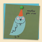 A blue bird wearing a party hat with  small green pom-pom. and the text 'Another Year Wiser' — Australian-made greeting card by Papernest