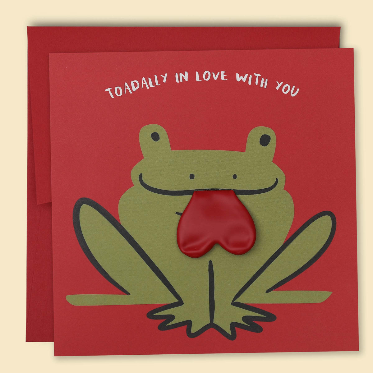 A greeting card with a frog illustration, with a real red heart balloon tongue inserted in its mouth, and the text 'TOADALLY IN LOVE WITH YOU' on the top. Australian-made greeting card by Papernest.